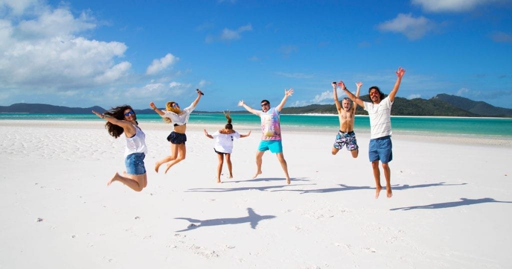 grupo de amigos saltando en la arena y detrás el agua cristalina de la playa